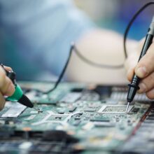 Closeup shot of male hands testing electric current voltage in circuit board of disassembled laptop using multimeter tool on table in maintenance shop